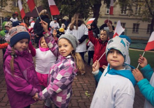 Dzieci z biało-czerwonymi flagami stoją na tarasie